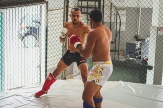 Two men engage in intense kickboxing sparring inside an MMA gym arena.